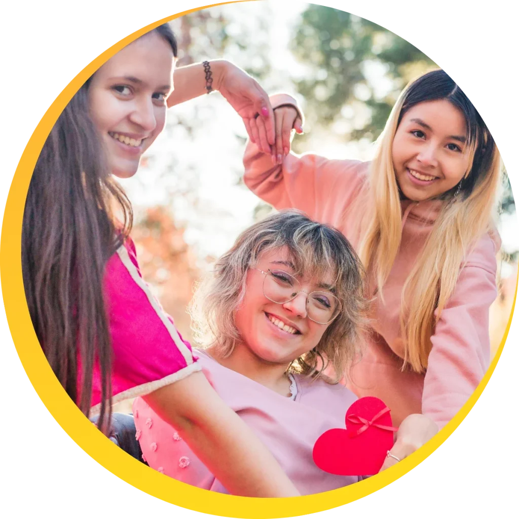 2 friends making a heart in front of a girl in wheel chair